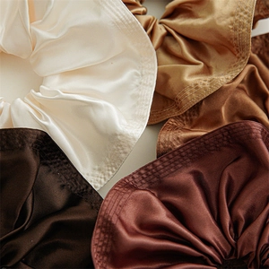 Macro detail of satin oversized scrunchies in coffee tones with fine stitching textures