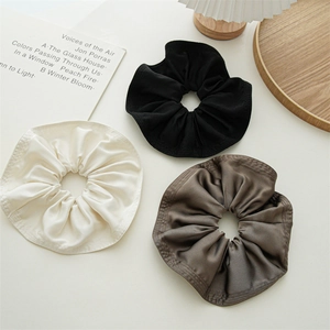 Three oversized satin scrunchies in black, cream, and brown displayed on a stylish tray