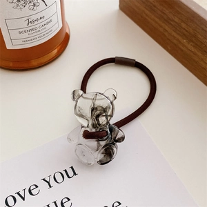 Close-up of a brown elastic hair tie featuring a transparent resin bear with ink texture