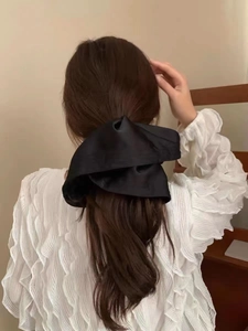 Rear view of a model wearing a large black satin scrunchie with elegant pleated details