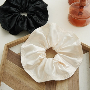 Detail of satin scrunchies in black and champagne on a wooden tray with elegant luster