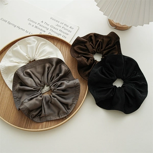 Detail of four silk-textured oversized hair scrunchies on a wooden tray with elegant folds