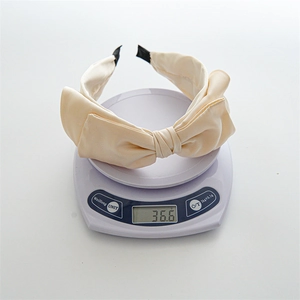 Cream satin oversized bow headband showing product weight of 36.6g on a digital scale