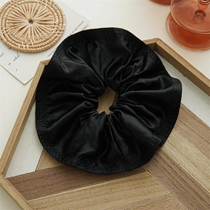 Close-up of a large black satin scrunchie with soft pleats on a wooden display tray