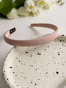 Detail of pink satin padded headband with handmade label on decorative ceramic plate