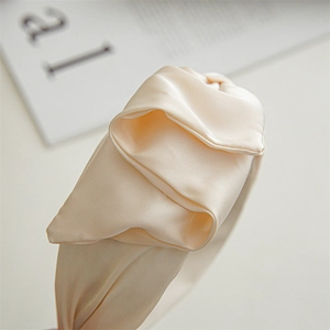 Close-up of champagne satin headband showing silk texture and elegant knot design detail
