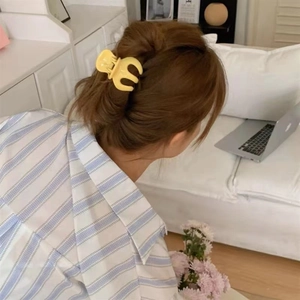 Pince à cheveux citrouille jaune mat fixant une queue de cheval sur cheveux bruns à la maison