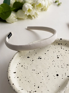 Detail of a beige padded headband with satin texture and a handmade label on a white tray