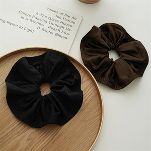 Detailed view of large satin scrunchies in black and brown colors on a wooden tray