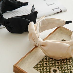 Close-up of black and cream satin wide bow headband with elegant pleated silk texture
