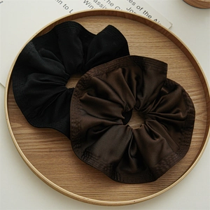 Close-up of black and dark brown satin scrunchies with ruffles on a wooden tray