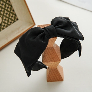 Detailed view of a black satin large bow headband on a geometric wooden stand