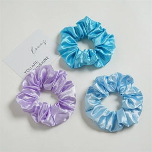 Close-up of three satin scrunchies in purple and blue with smooth glossy texture