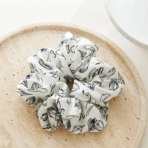 Detail eines weißen Scrunchie mit schwarzen Blattmustern auf einem beigen Steintablett