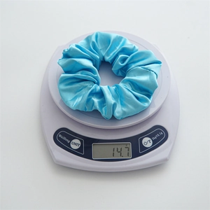 Detailed close-up of a blue LED satin scrunchie being weighed on a digital scale