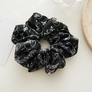 Nahaufnahme eines schwarzen Satin-Scrunchie mit weißen Blattmustern auf minimalistischer Fläche