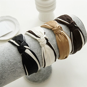 Satin fabric knotted headbands in black, white and khaki displayed on a grey stand