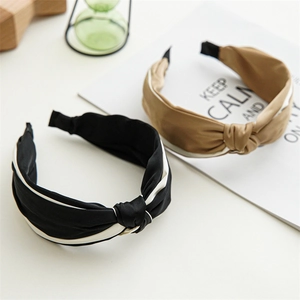 Detail of cross knot satin headbands in black and beige with elegant contrast piping