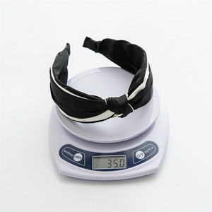 Cross knot wide headband in satin fabric with contrast white trim on a digital scale