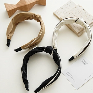 Close-up of knotted satin headbands in khaki, cream and black on a minimalist display