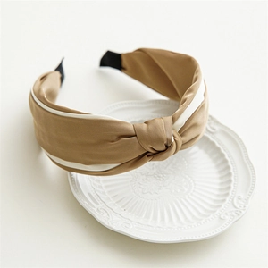 Close-up detail of a khaki satin knotted headband with white trim on a white ceramic plate