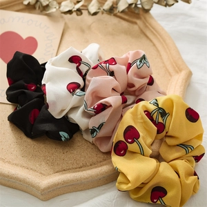 Detailed view of four colorful cherry print chiffon scrunchies on a decorative tray