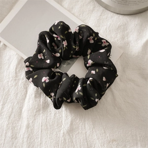 Close-up detail of a black floral chiffon scrunchie with delicate pink flower patterns