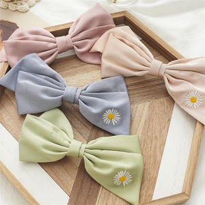 Detailed embroidery of white daisy on fabric bow hair clips in pastel color variations