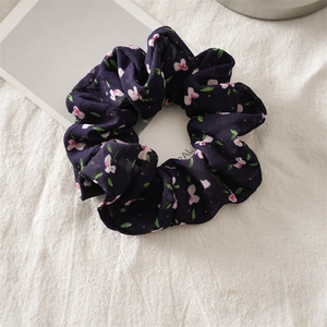 Close-up of chiffon floral scrunchie with pink flowers on a deep purple fabric