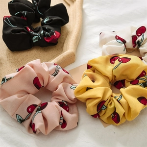 Close-up of four cherry-printed chiffon scrunchies in black white pink and yellow