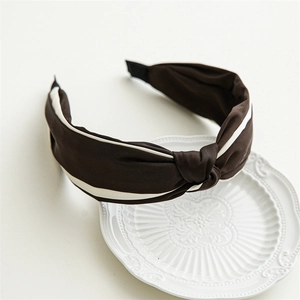 Detail of dark brown satin knot headband with white stripe edges on decorative plate