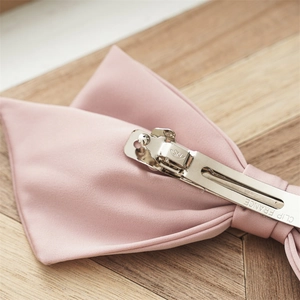 Pink satin bow hair clip with daisy embroidery on a natural wood texture background