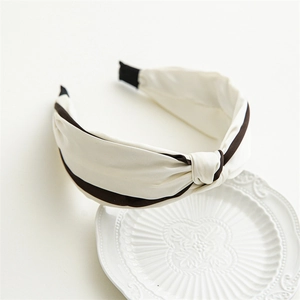Close-up of beige satin knotted headband with dark stripes on a white ceramic plate