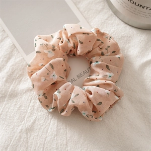 Detailed view of floral chiffon scrunchie with peach flower patterns on soft white fabric