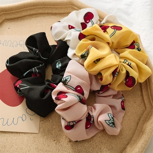 Close-up of four cherry print scrunchies in black, pink, yellow, and white on a tray