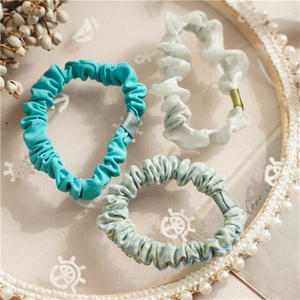 Close-up of three aesthetic scrunchies in blue and green fabric on a lace tray