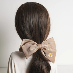 Detail of champagne satin bow hair clip with daisy embroidery on a low ponytail
