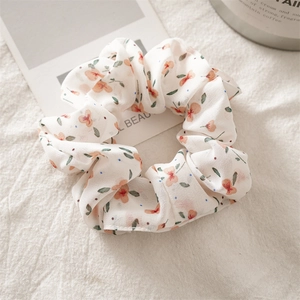 Close-up of chiffon floral scrunchie with orange flower prints on soft white background