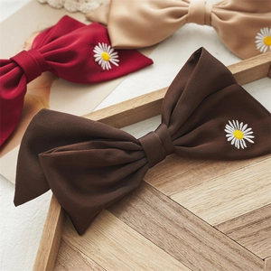 Close-up of elegant bow hair clips with delicate daisy embroidery on premium textured fabric