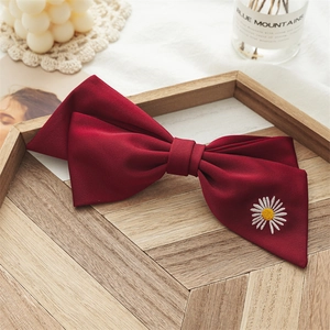 Detail of burgundy hair bow clip featuring a delicate white daisy flower embroidery