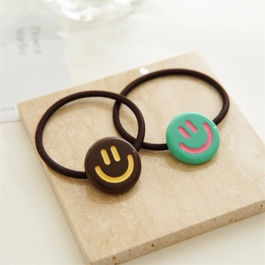 Close-up of two elastic hair ties with cute resin smiley face charms on a stone board