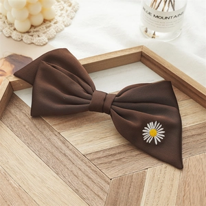 Detail of coffee brown bow hair clip with white daisy embroidery on a wooden tray