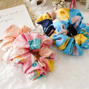 Close-up of two fabric scrunchies with vibrant floral and geometric prints on white fabric