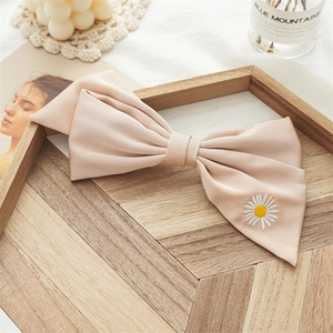 Close-up of a chiffon bow hair clip featuring delicate white daisy embroidery detail