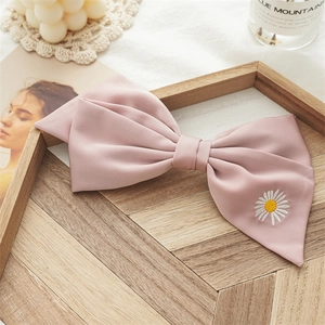 Detailed shot of a pink satin bow hair clip with small daisy embroidery on wood