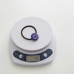 Detail view of a 4.5g brown elastic hair tie with a blue smiley face charm on a scale