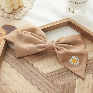 Macro shot of khaki matte satin bow hair clip featuring delicate daisy embroidery detail