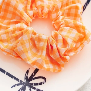 Close-up of orange and white checkered scrunchie with soft fabric texture in a white tray