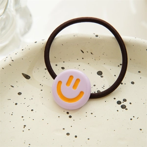 Detail of cute purple smiley face charm on a high elasticity black hair tie in a ceramic tray