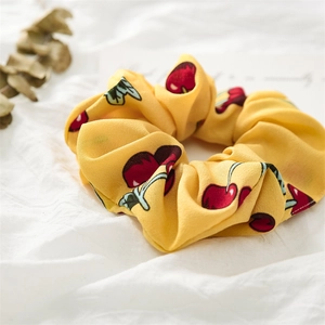 Detail of yellow cherry print chiffon scrunchie on white fabric with artistic card